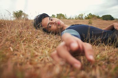 Portrait of young man lying on grassy field against sky