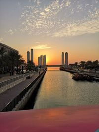 Sea by buildings against sky during sunset