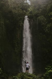 Man standing by waterfall in forest against sky