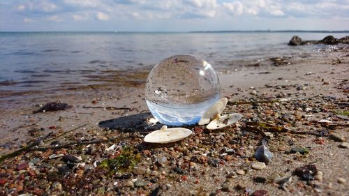 Close-up of crystal ball on beach against sky