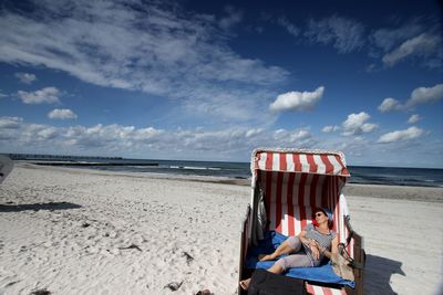 Full length of woman relaxing in hooded chair at beach on sunny day