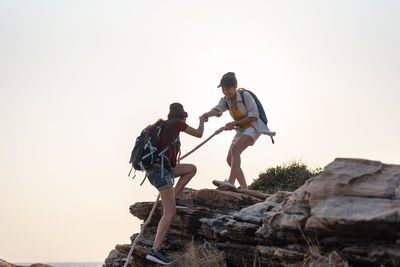 Low angle view of men standing on rock against sky