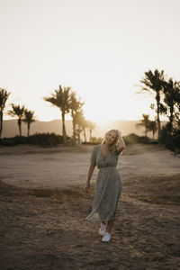 Woman standing on road amidst trees on field against sky