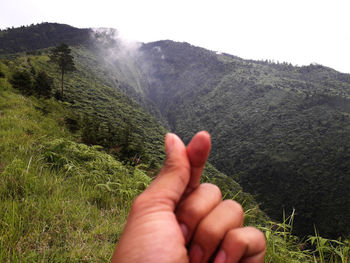 Cropped image of person hand on mountain against sky