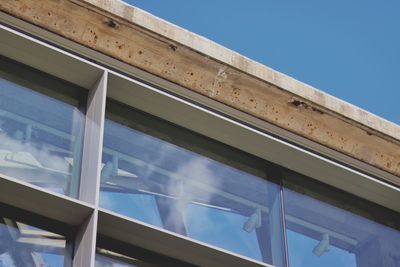 A concrete and glass building against a clear blue sky with lights visible through the glass