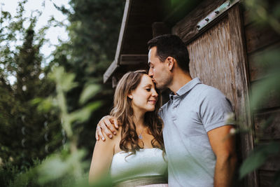 Low angle view of romantic couple standing against trees at park