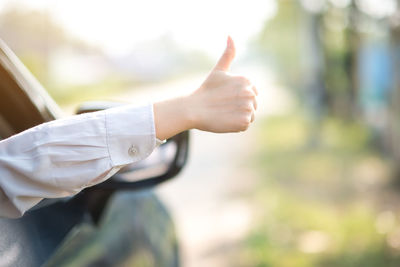 Cropped hands of woman gesturing thumbs up sign while sitting in car