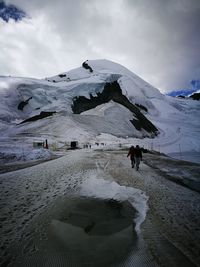 People walking on snowcapped mountain against sky