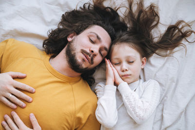 Young sleeping family with bearded father and daughter on bed in home, view from top