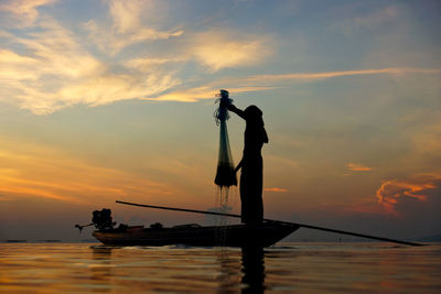 Silhouette people standing by sea against sky during sunset