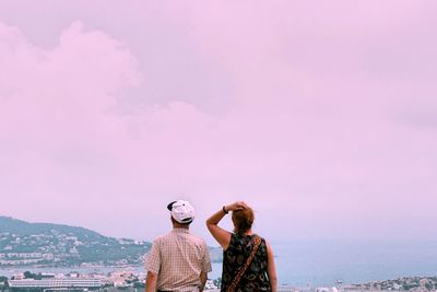 People standing by pink sea against sky in city