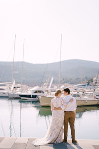 Rear view of friends standing on shore against sky
