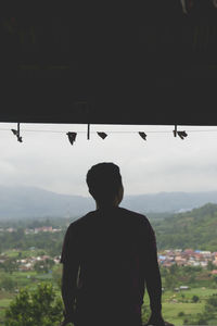 Rear view of silhouette man looking at city against sky