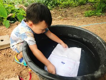 Boy putting book in bucket with water on field