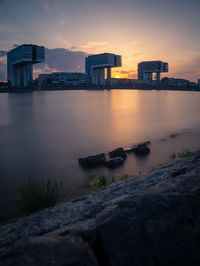 Scenic view of river by buildings against sky at sunset