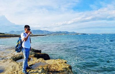 Man standing on rock by sea against sky
