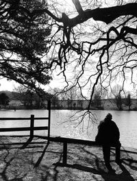 Rear view of silhouette man standing by railing against lake