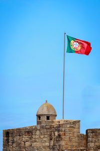 Low angle view of flag against building against clear blue sky