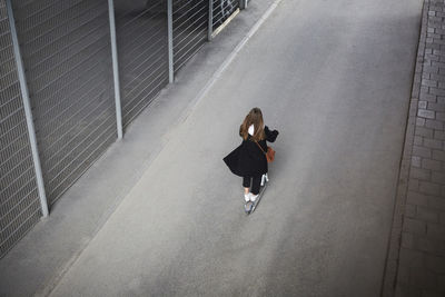 Rear view of teenage girl riding electric push scooter on street in city