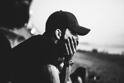 Side view of man yawning while sitting against sky