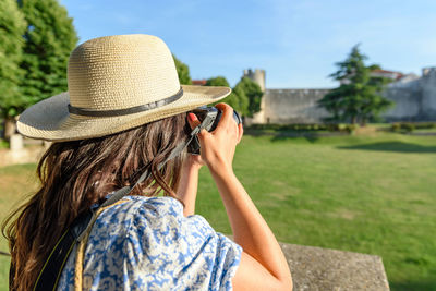 Rear view of young woman using dslr camera to take photos of a village on a sunny summer day