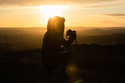 Silhouette woman photographing against sky during sunset