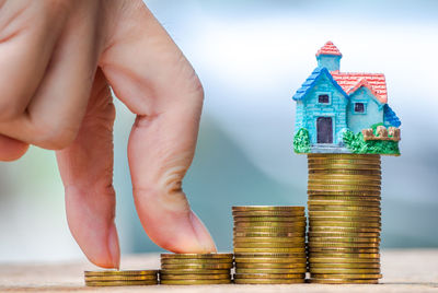 Cropped image of hand with stacked coins and model house on table 