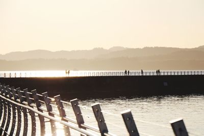 Pier over river against clear sky during sunset