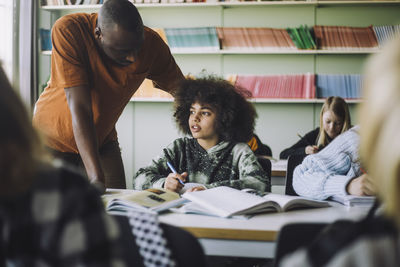 Male teacher helping student while studying in classroom