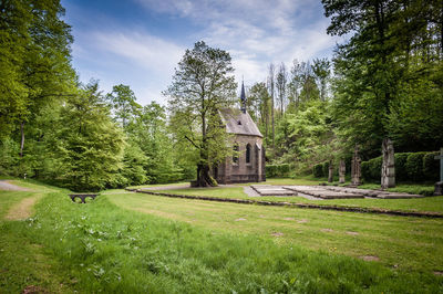 Chapel in cemetery amidst trees against sky on sunny day