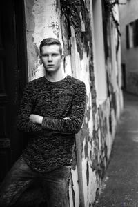 Portrait of young man with arms crossed standing against weathered wall