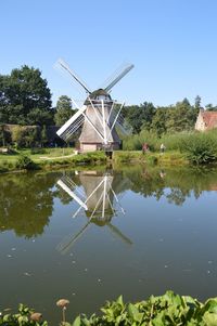 Traditional windmill by lake against sky