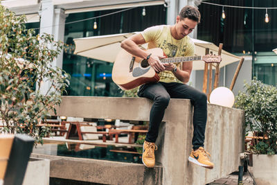 Young man playing guitar while sitting on railing