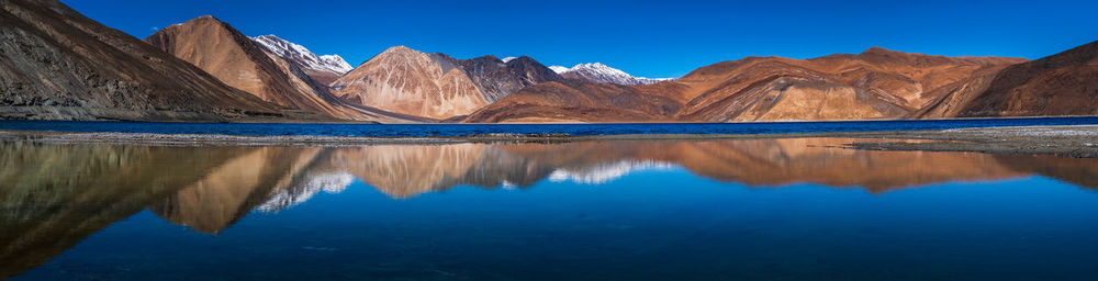 Reflection of mountain range in lake against clear blue sky