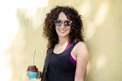 Portrait of young woman wearing sunglasses against wall