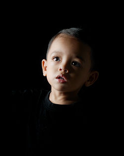 Close-up portrait of cute boy against black background