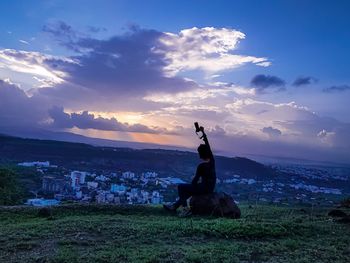 People sitting on field against sky during sunset