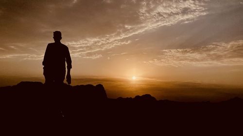 Rear view of silhouette man standing on rock against sky during sunset