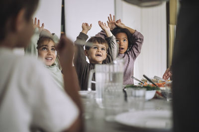 Happy children with arms raised during lunch time at kindergarten