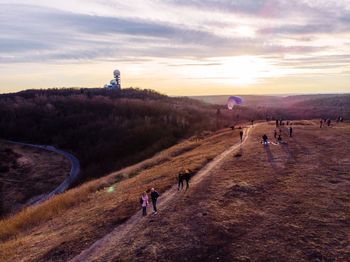 High angle view of people walking on mountain against cloudy sky during sunset