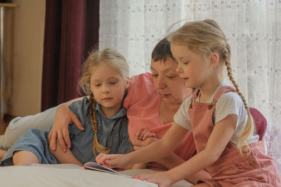 Full length of grandmother with granddaughters reading book at home