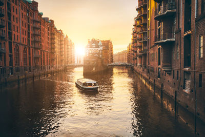 Canal amidst buildings in city during sunset