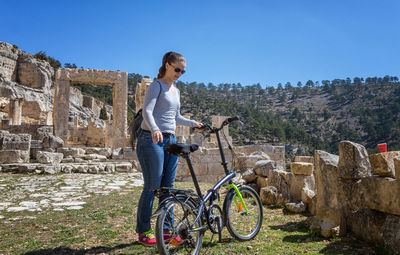 Woman standing with bicycle on field against clear sky