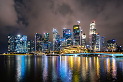 Illuminated city by river against sky at night