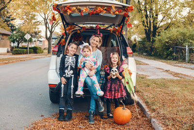Portrait of smiling family in car on road against trees