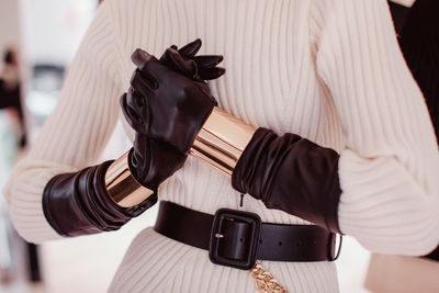 Knitted white sweater, black leather gloves, belt, gold bracelets. fashion accessories