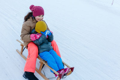 Two children sledding on snow slope at wooden sleigh