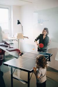 Boy looking at female professionals playing table tennis in creative office