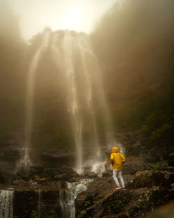 Rear view of man standing against waterfall