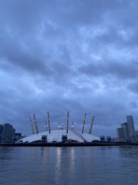 Cranes at waterfront against cloudy sky